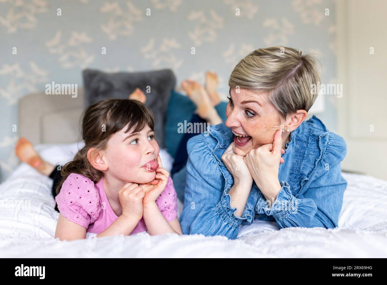 Fröhliche Mutter und Tochter machen Gesichtsausdruck auf dem Bett liegend Stockfoto