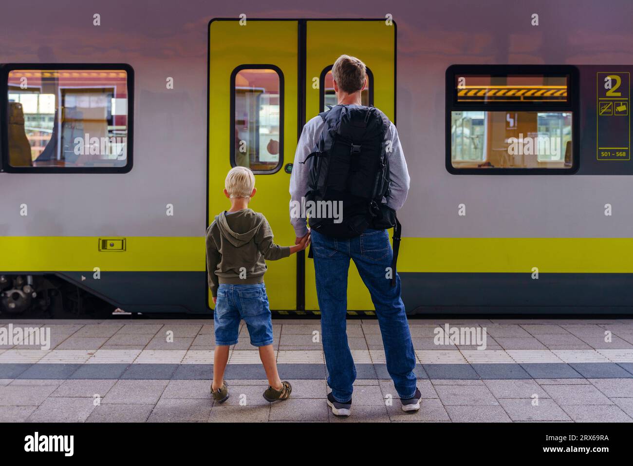 Der Vater hält die Hände mit dem Sohn, der vor dem Zug steht Stockfoto