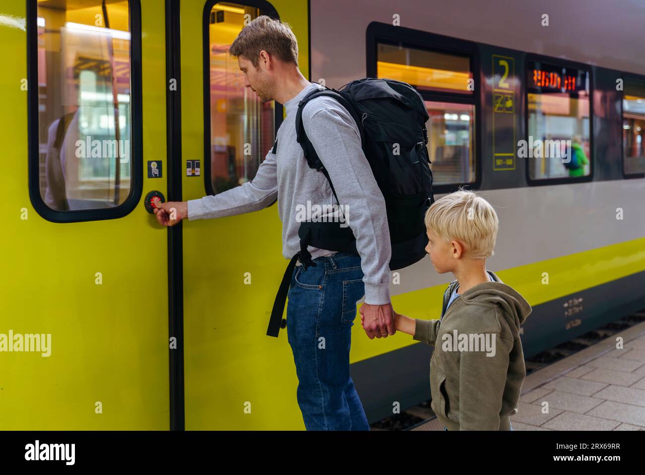 Mann, der die Tür des Zuges öffnet und die Hände mit dem Sohn am Bahnhof hält Stockfoto