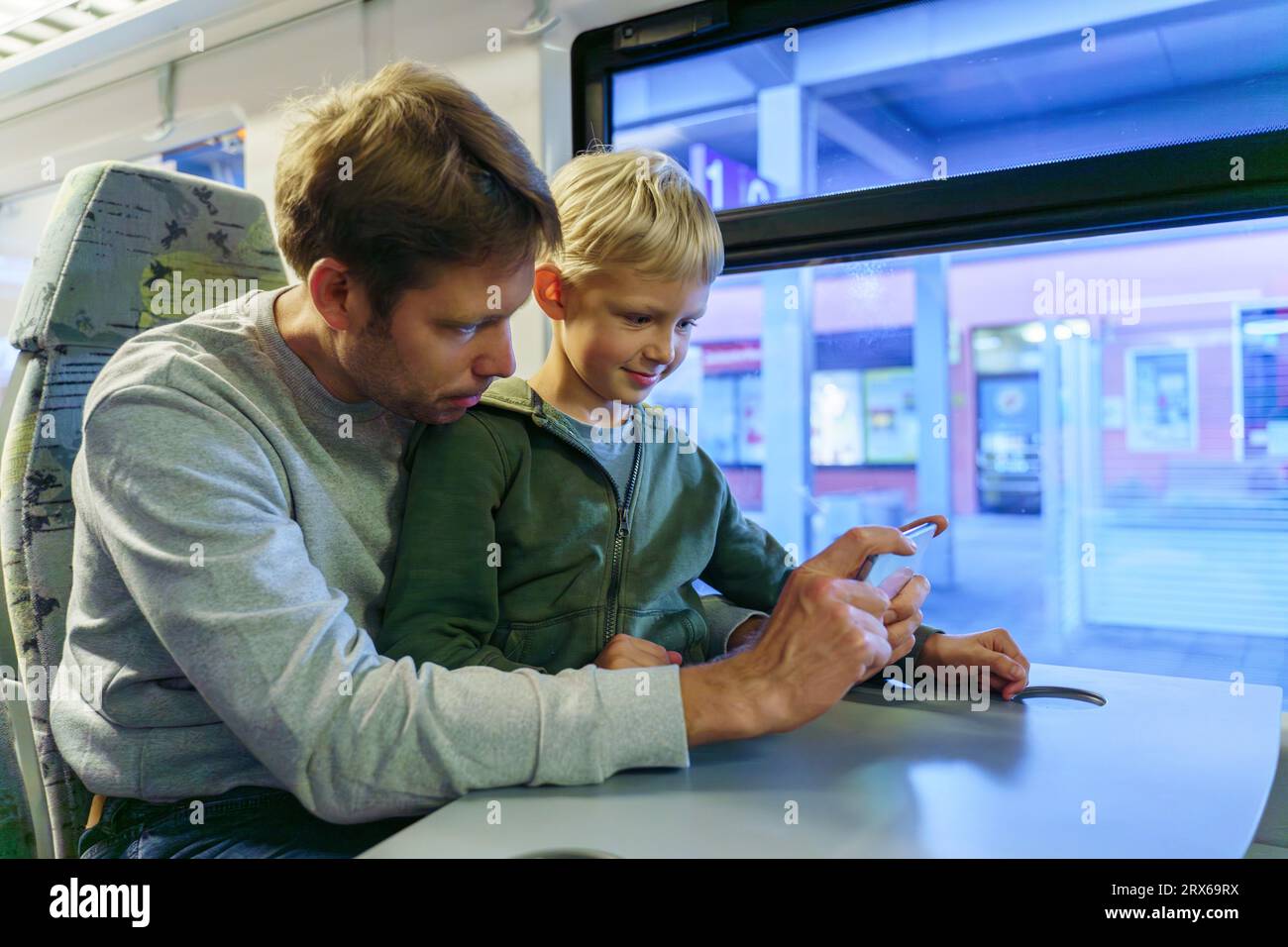 Lächelnder Junge mit Vater, der Smartphone in der Nähe des Fensters im Zug benutzt Stockfoto