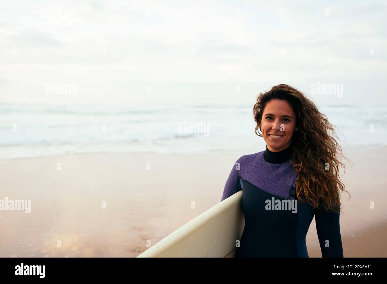 Glückliche junge Frau mit Surfbrett am Strand im Urlaub Stockfoto