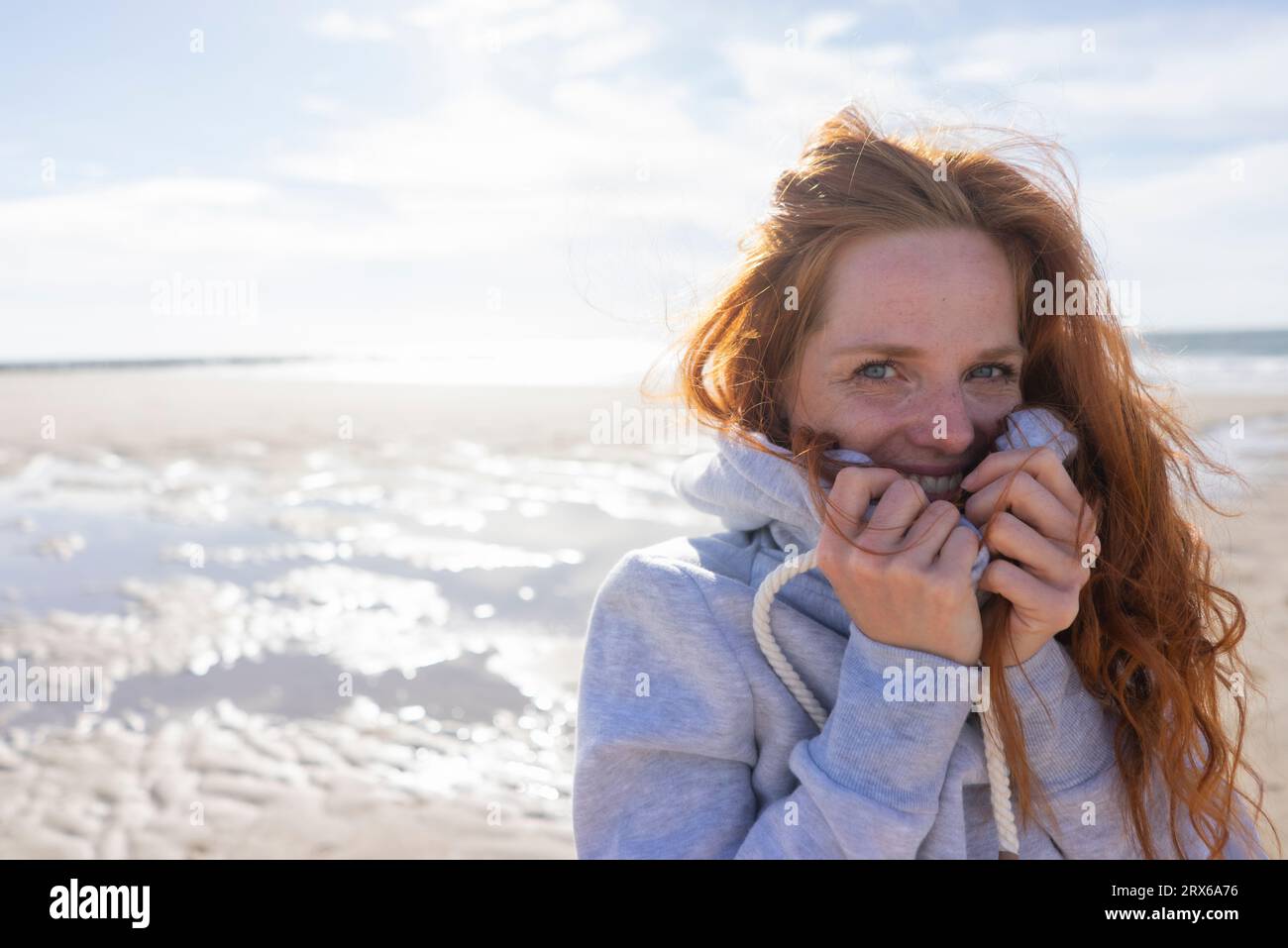 Rothaarige Frau, die das Gesicht in einem Kapuzenhemd am Strand bedeckt Stockfoto