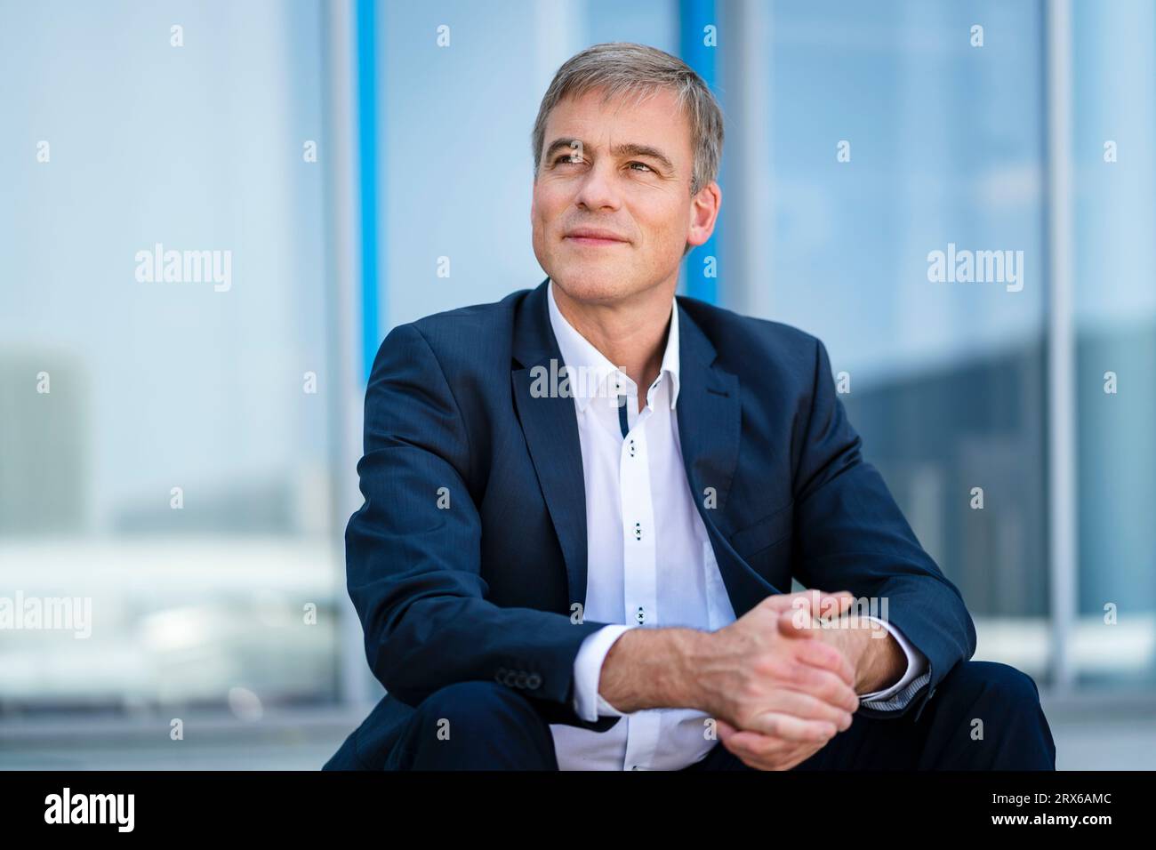 Ruhiger Geschäftsmann, der vor dem modernen Bürogebäude sitzt Stockfoto