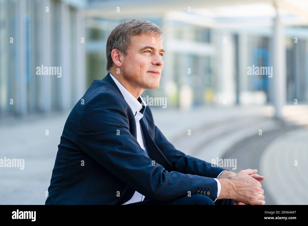 Ruhiger Geschäftsmann, der vor dem modernen Bürogebäude sitzt Stockfoto