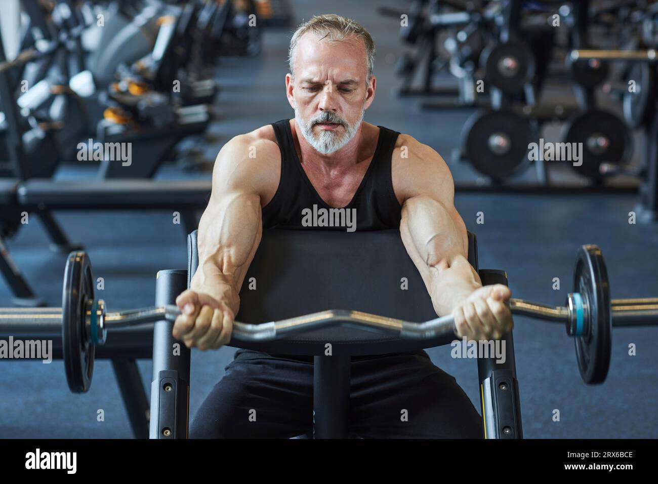 Reifer Mann, der die Arme mit Langhantel im Fitnessstudio stärkt Stockfoto