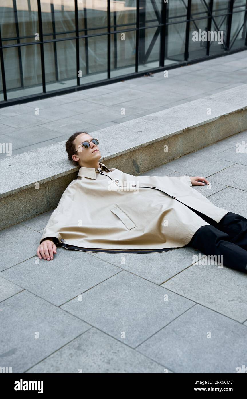 Androgyner Mann, der Poncho trägt und auf einer Betonstraße in der Stadt schläft Stockfoto
