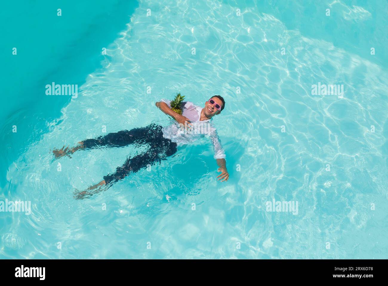 Glücklicher Mann, der mit Ananas im Pool schwimmt Stockfoto