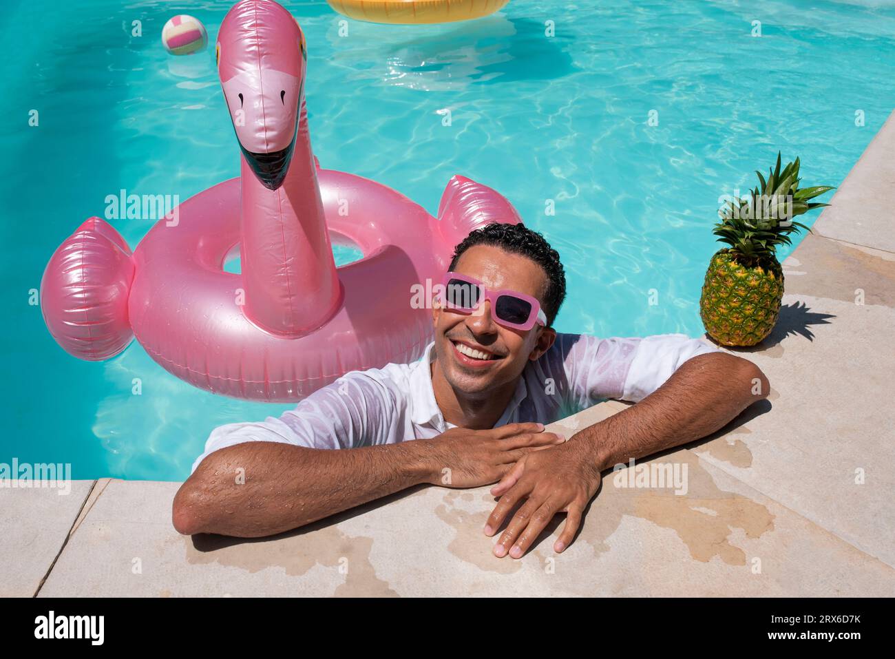 Glücklicher Mann mit Ananas und aufblasbarem Schwimmring am Pool Stockfoto