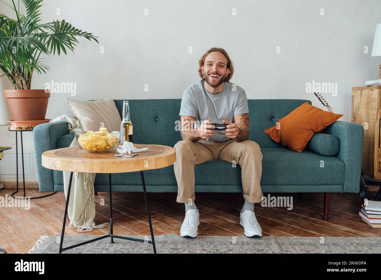 Glücklicher junger Mann, der zu Hause Videospiele auf dem Sofa spielt Stockfoto