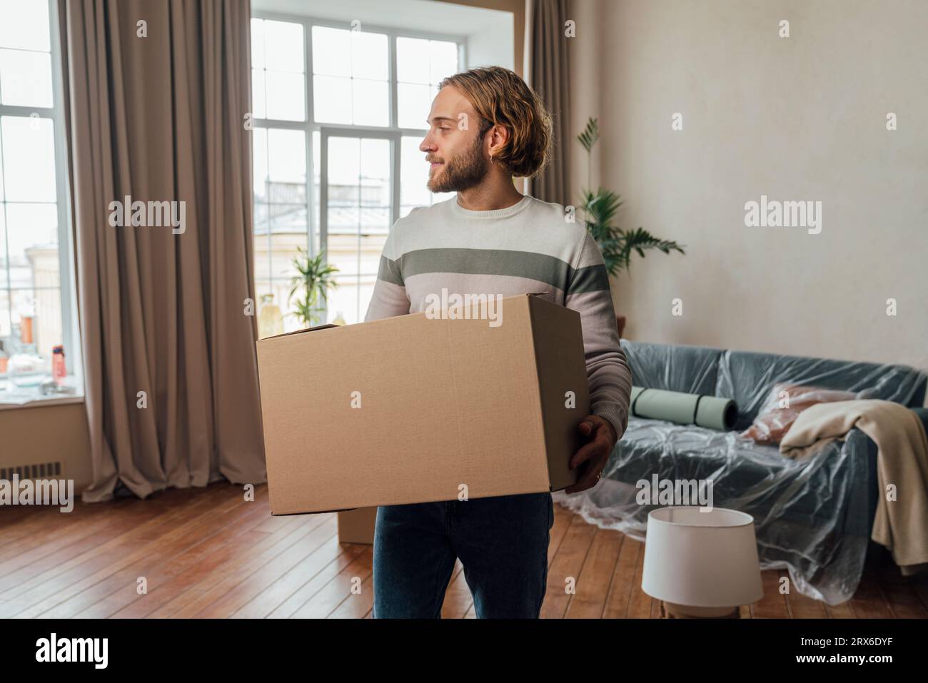 Junger Mann mit Pappkarton im Wohnzimmer Stockfoto