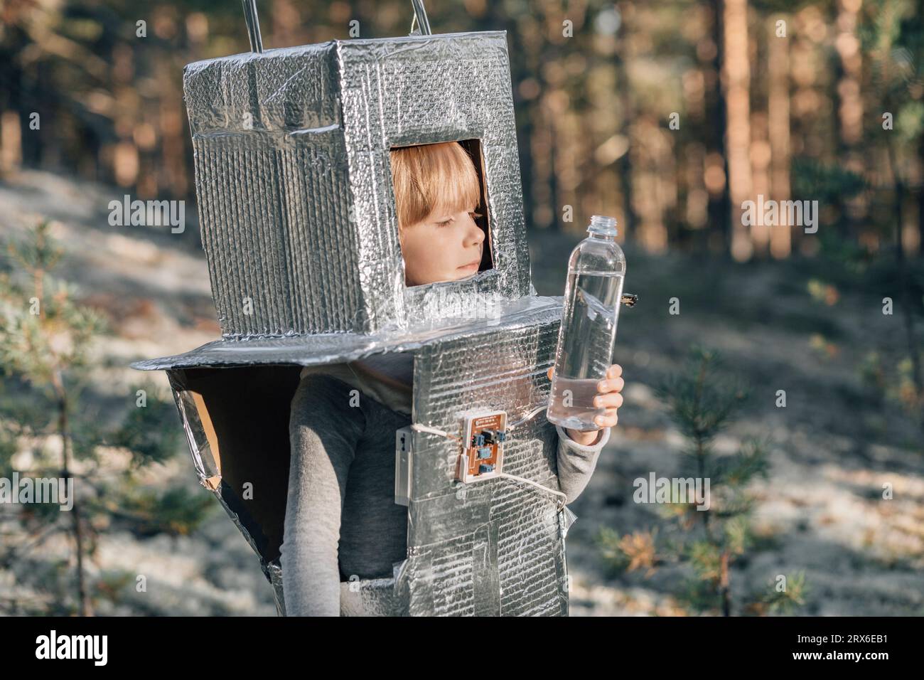 Junge im Astronautenkostüm und mit Wasserflasche im Wald Stockfoto