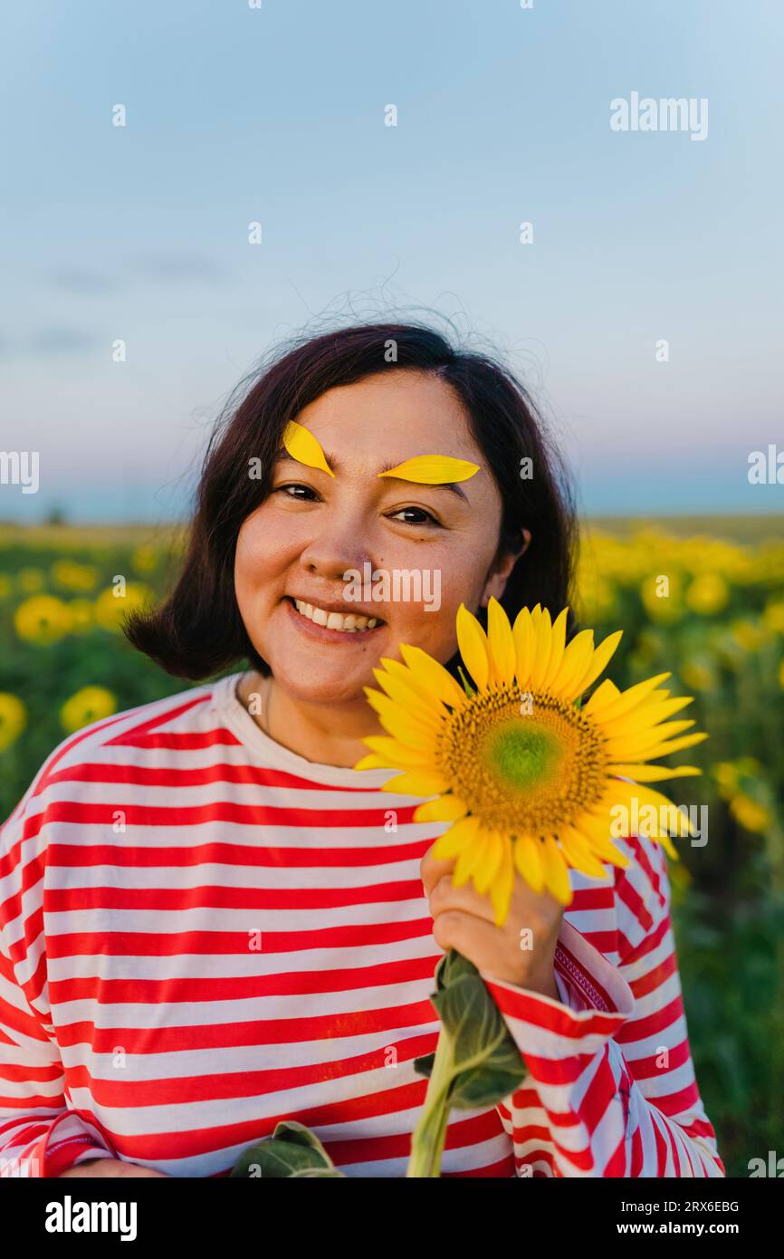 Lächelnde Frau mit Sonnenblumenblättern auf Augenbrauen auf dem Feld Stockfoto