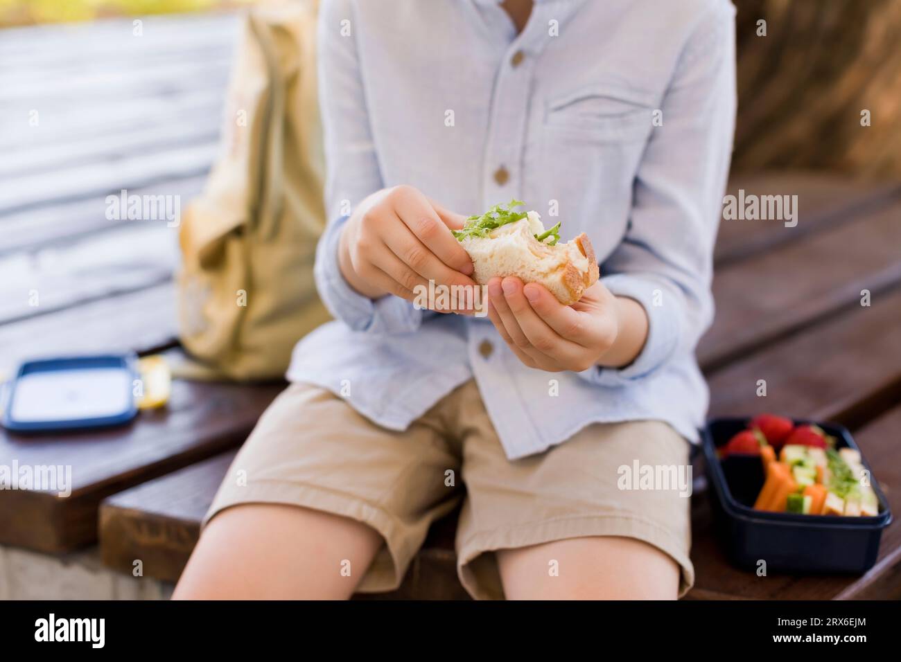 Junge, der Sandwich hält und auf der Bank sitzt Stockfoto