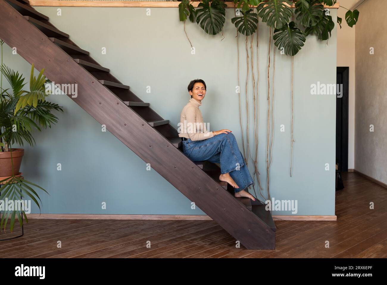 Glückliche Frau, die zu Hause auf einer Holztreppe sitzt Stockfoto