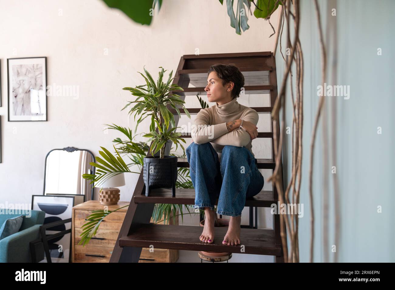 Nachdenkliche Frau mit gekreuzten Armen, die zu Hause auf der Treppe sitzt Stockfoto