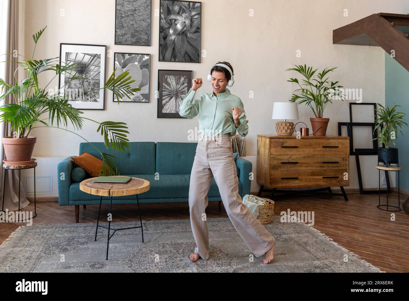 Glückliche Frau, die kabellose Kopfhörer trägt und zu Hause im Wohnzimmer tanzt Stockfoto