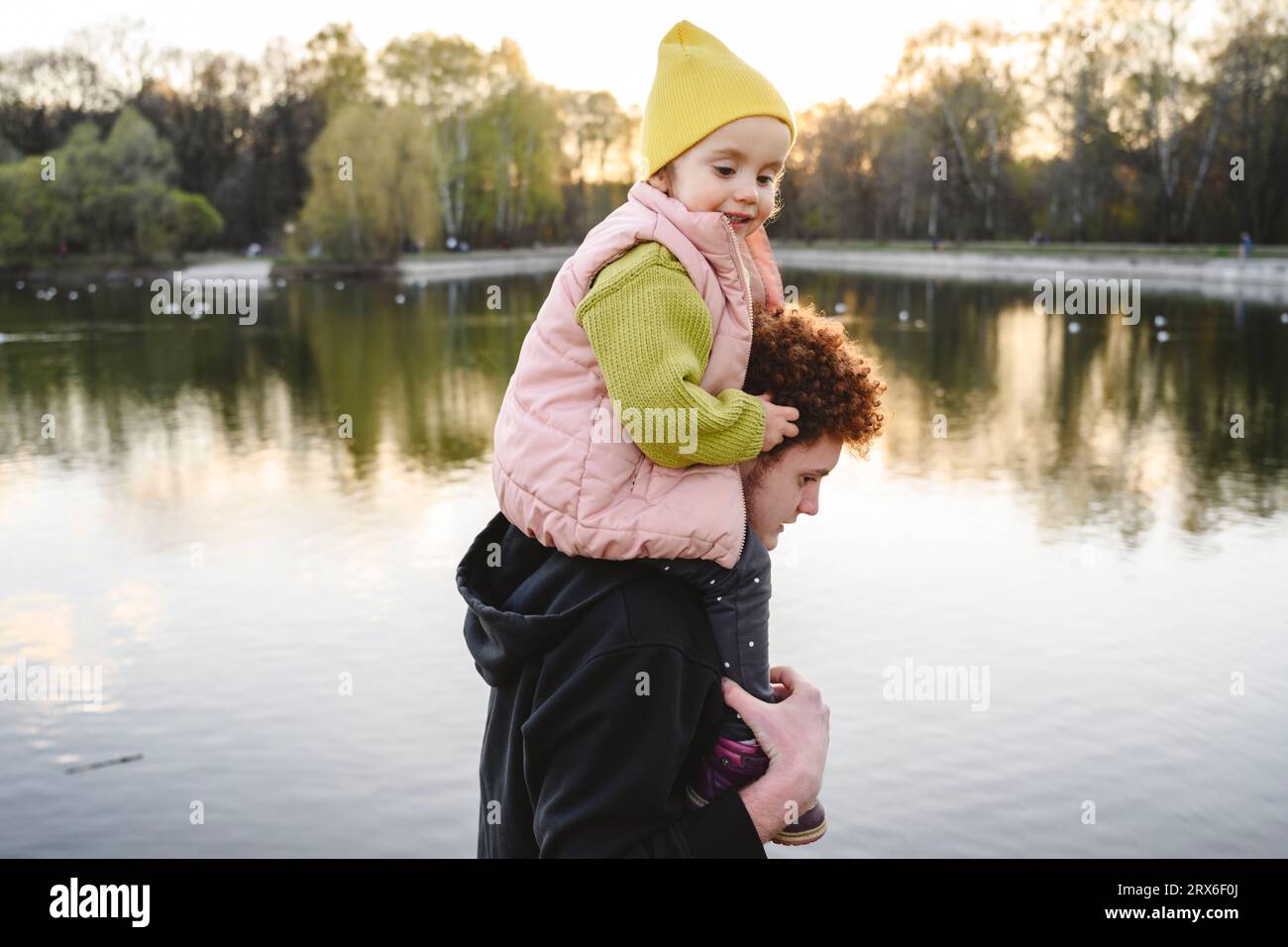Bruder trägt Schwester auf den Schultern am See im Park Stockfoto