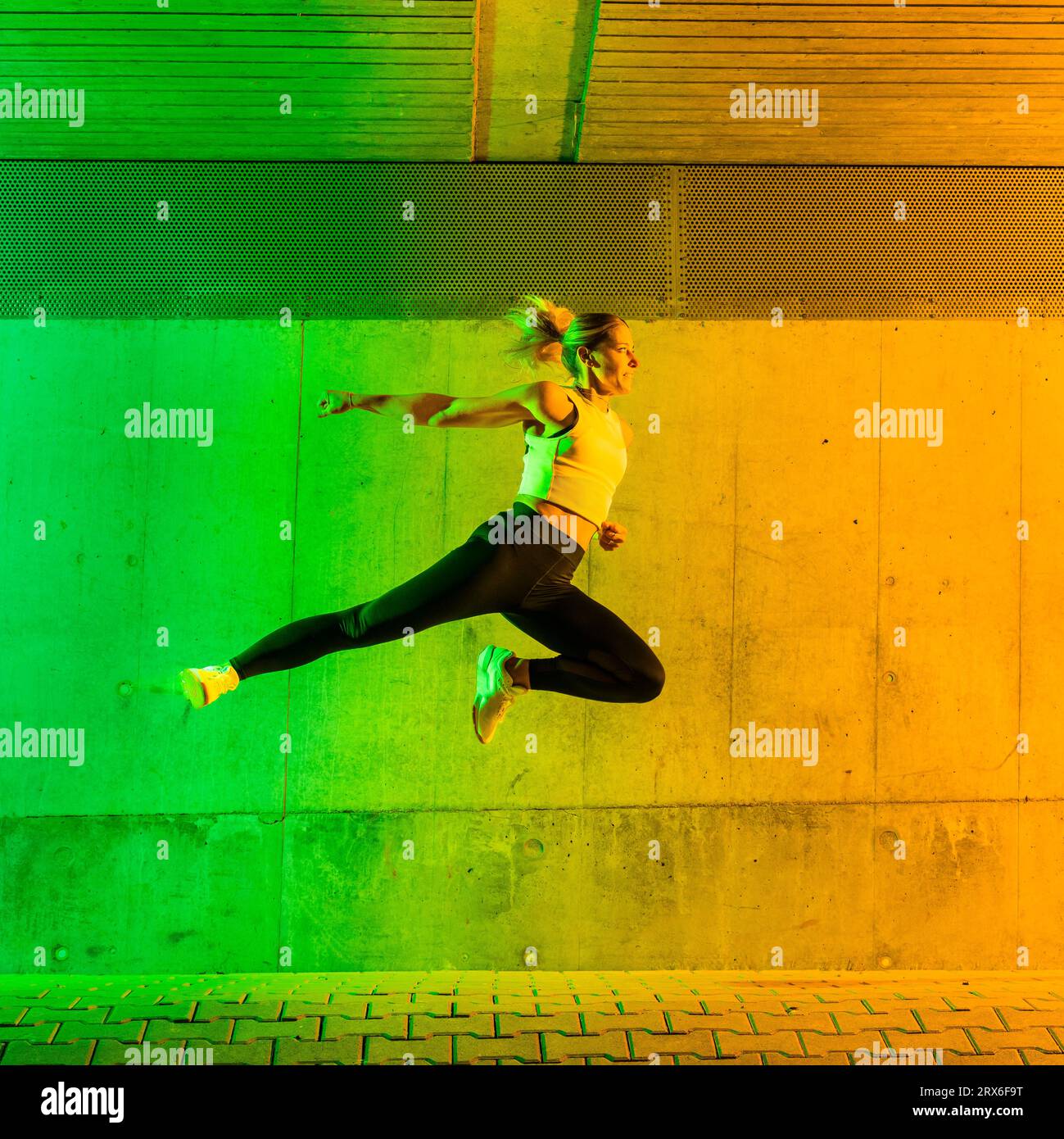 Frau, die Sportkleidung trägt, springt in der Nähe einer neonfarbenen Wand Stockfoto