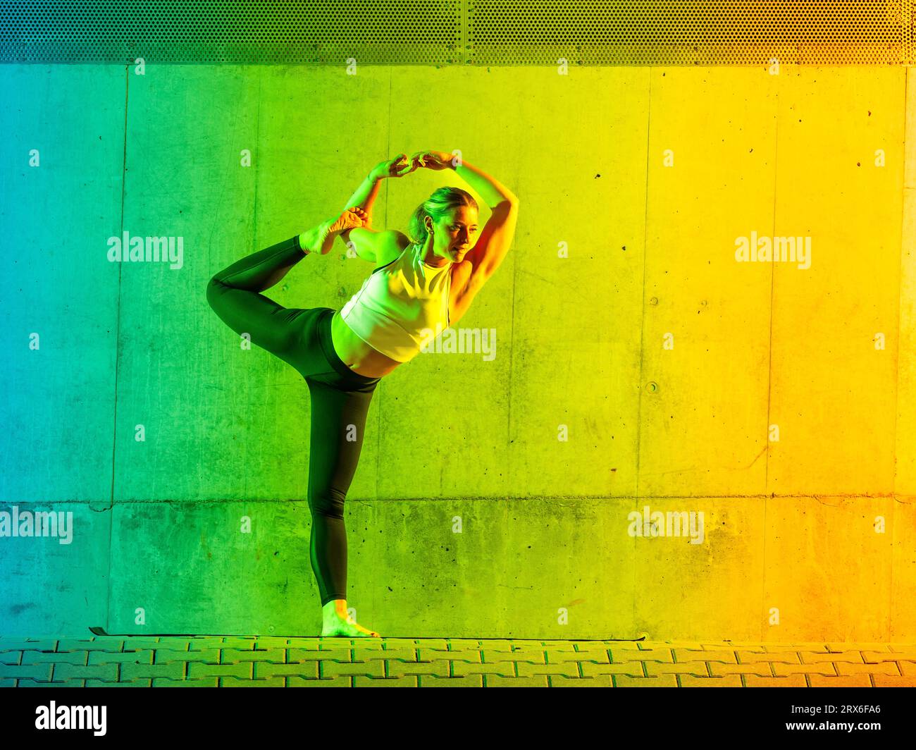 Frau, die Yoga macht, trägt Sportswear vor einer neonfarbenen Wand Stockfoto