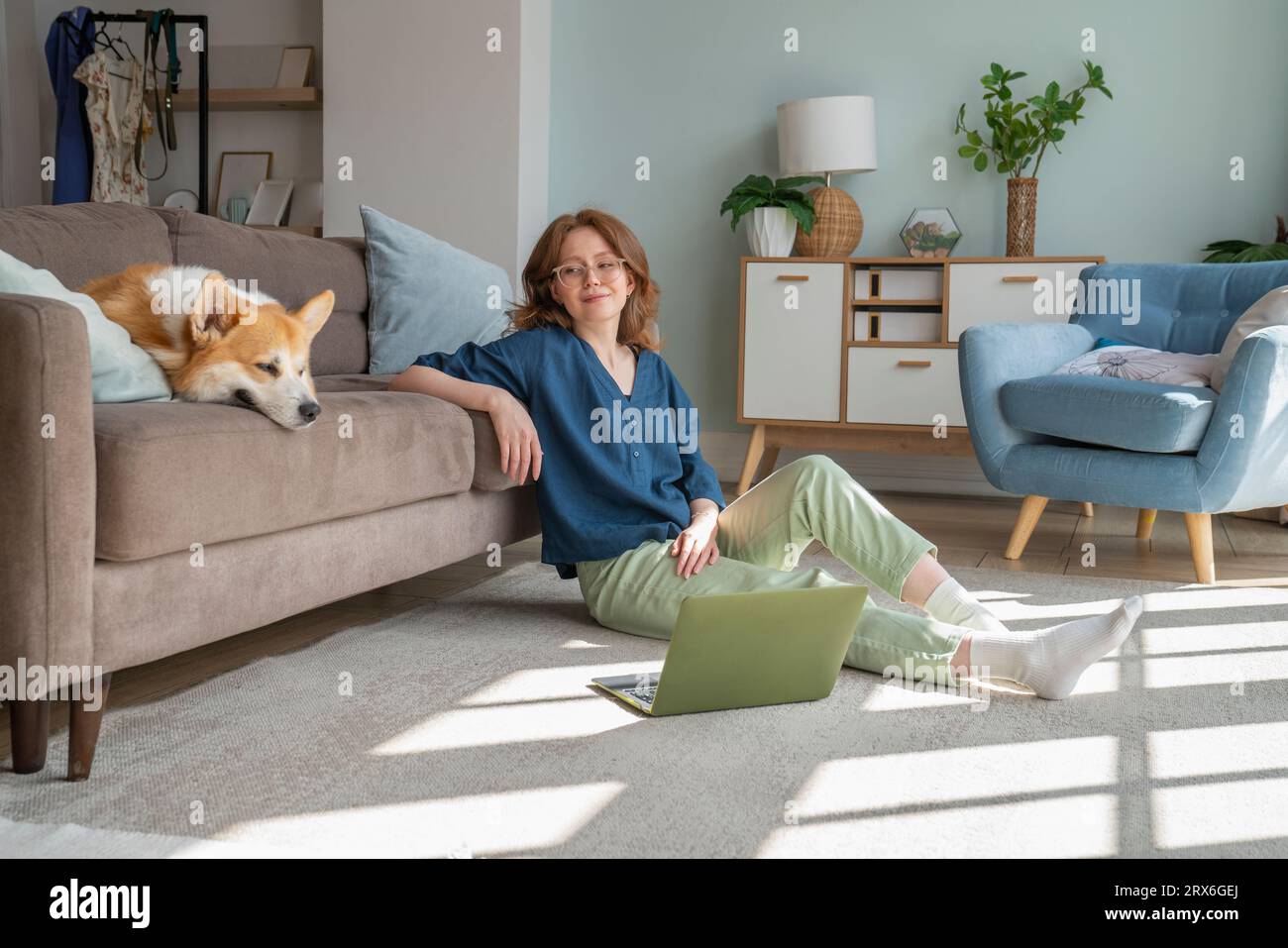 Junge Frau, die Waliser Corgi-Hund auf dem Sofa im Wohnzimmer ansieht Stockfoto