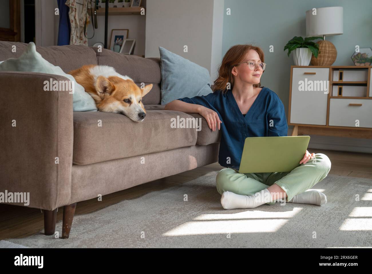 Junger Freiberufler mit Laptop, der von einem Hund im Wohnzimmer sitzt Stockfoto