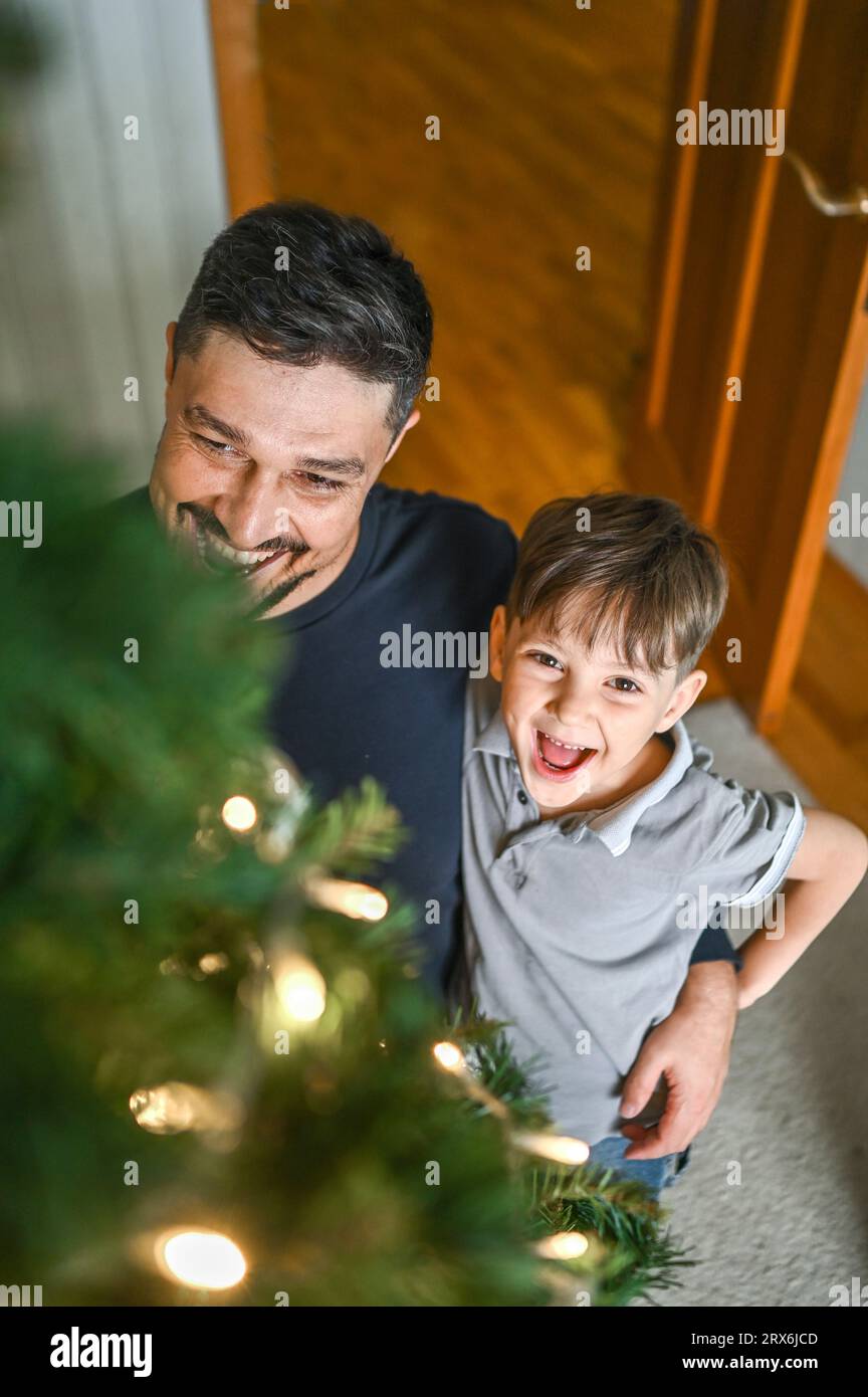 Lächelnder Vater und Sohn mit Blick auf den geschmückten Weihnachtsbaum Stockfoto