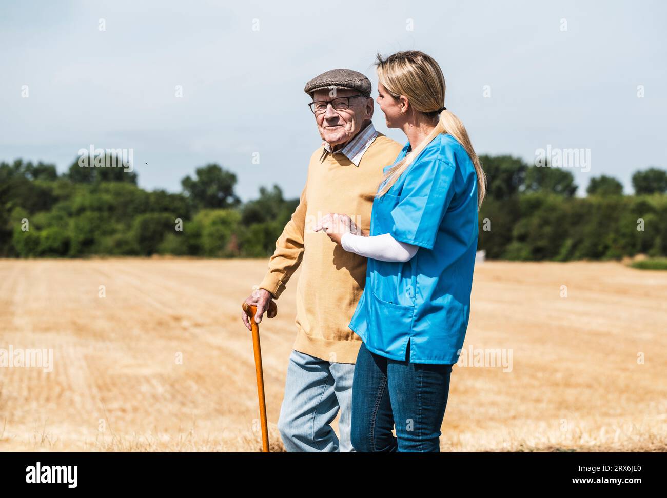 Pflegekräfte, die die Hand des älteren Mannes halten und auf dem Feld gehen Stockfoto
