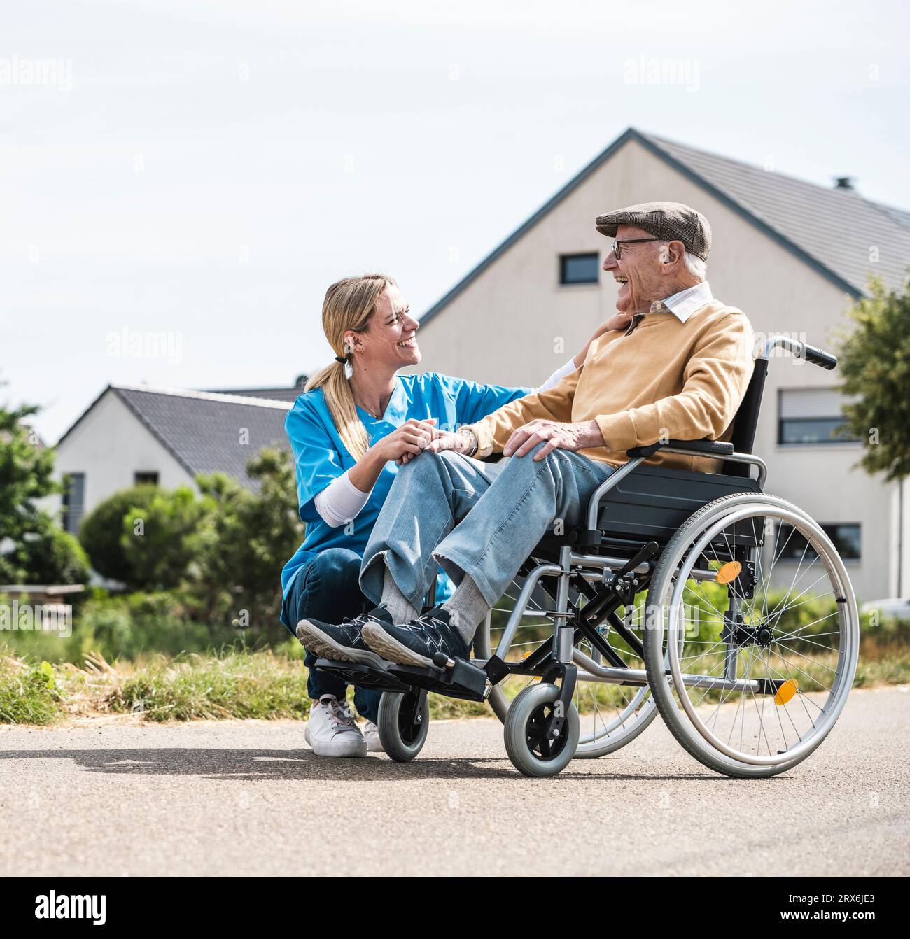 Lächelnde Krankenschwester, die mit einem älteren Mann spricht, der am sonnigen Tag im Rollstuhl sitzt Stockfoto