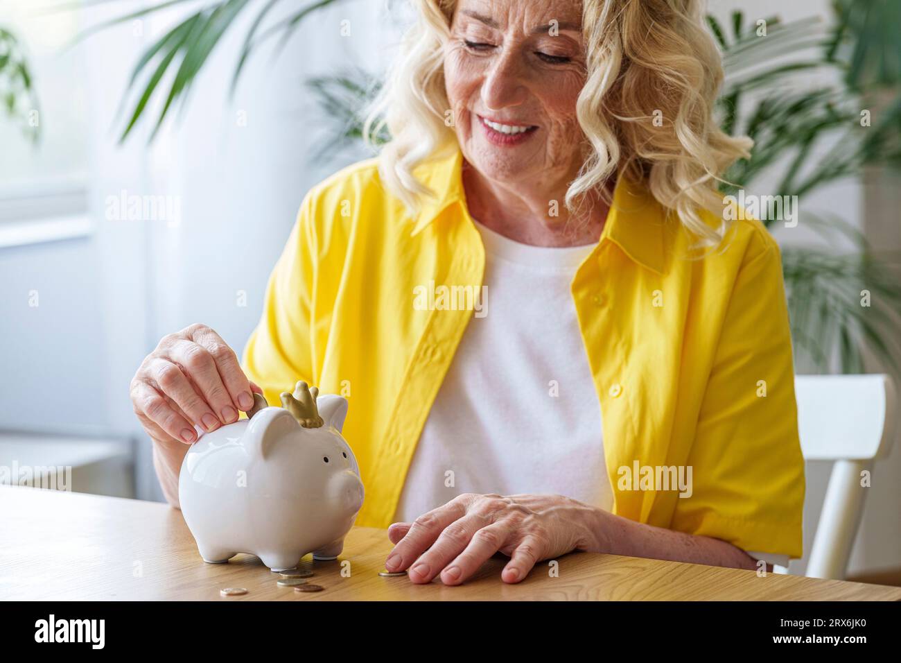 Glückliche Seniorin, die Geld in der Schweinebank spart Stockfoto