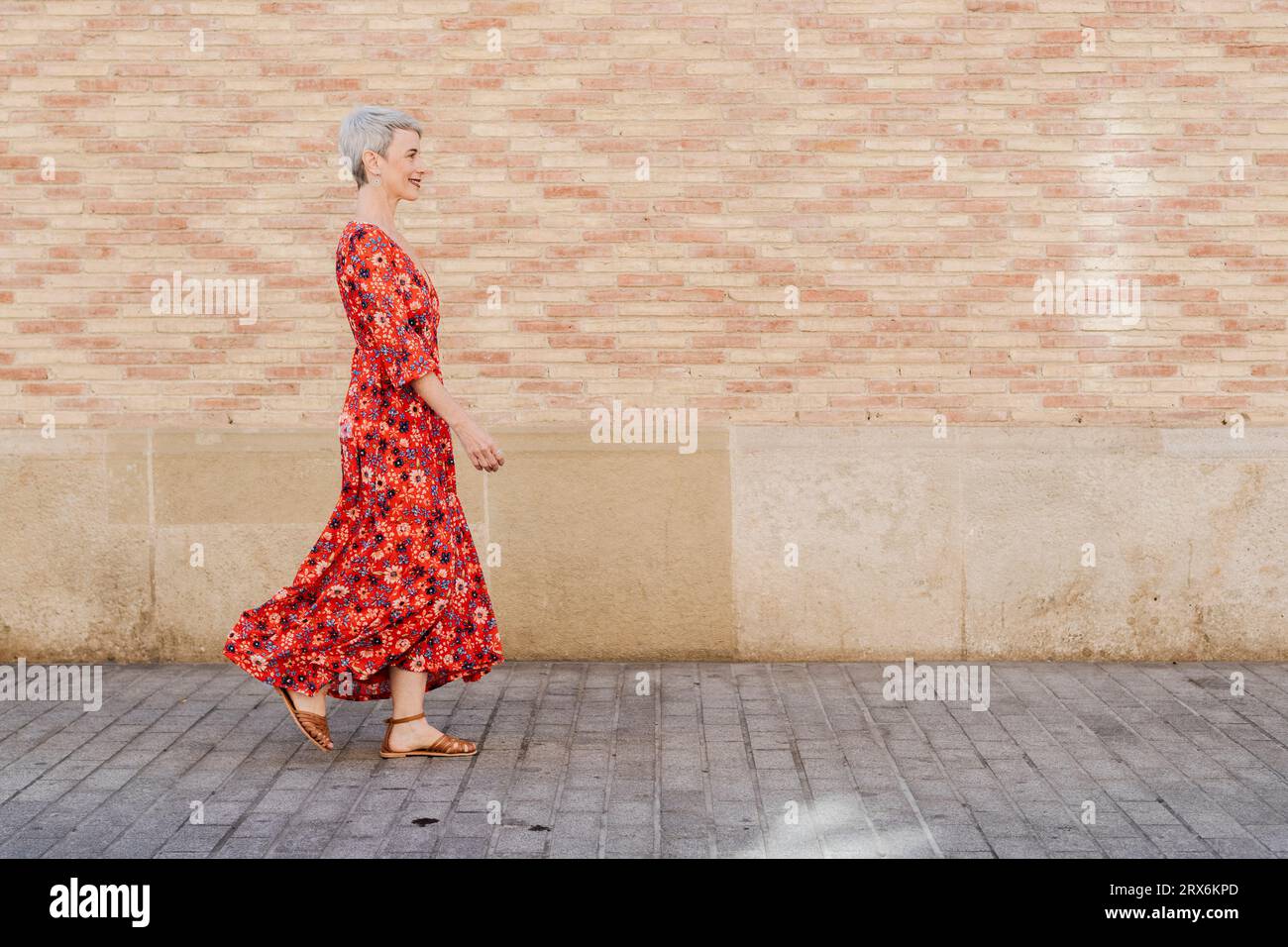 Lächelnde Frau in rotem Kleid, die vor der Wand läuft Stockfoto