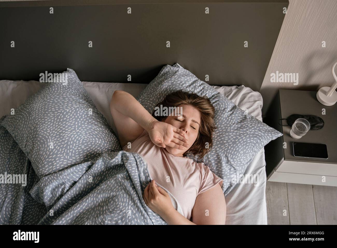 Junge Frau, die zu Hause auf dem Bett gähnt Stockfoto