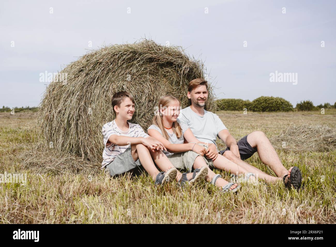 Lächelnde Kinder sitzen mit Vater in der Nähe von Heu auf dem Feld Stockfoto