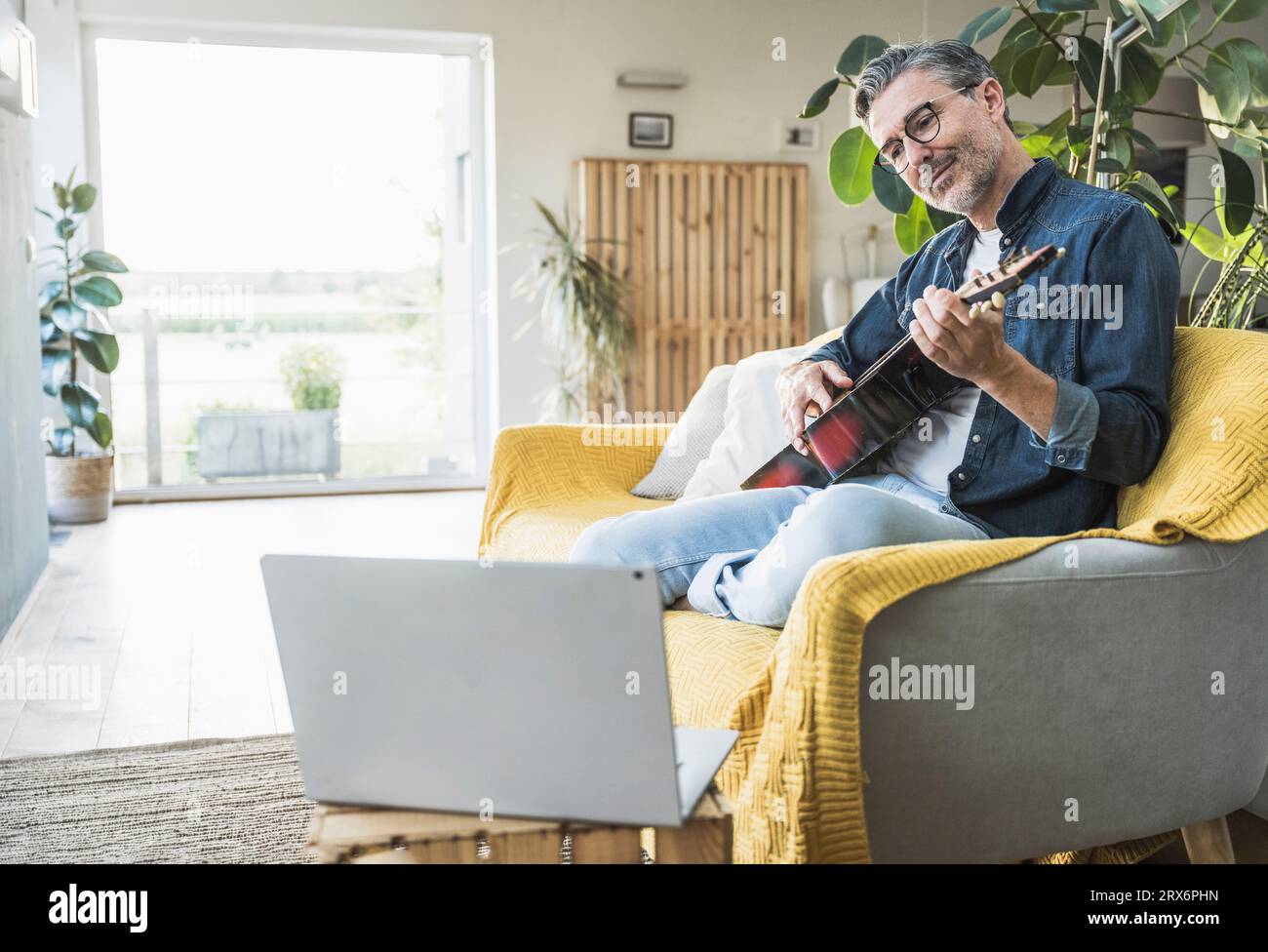 Mann, der Gitarre spielt, schaut sich das Tutorial auf dem Laptop zu Hause an Stockfoto