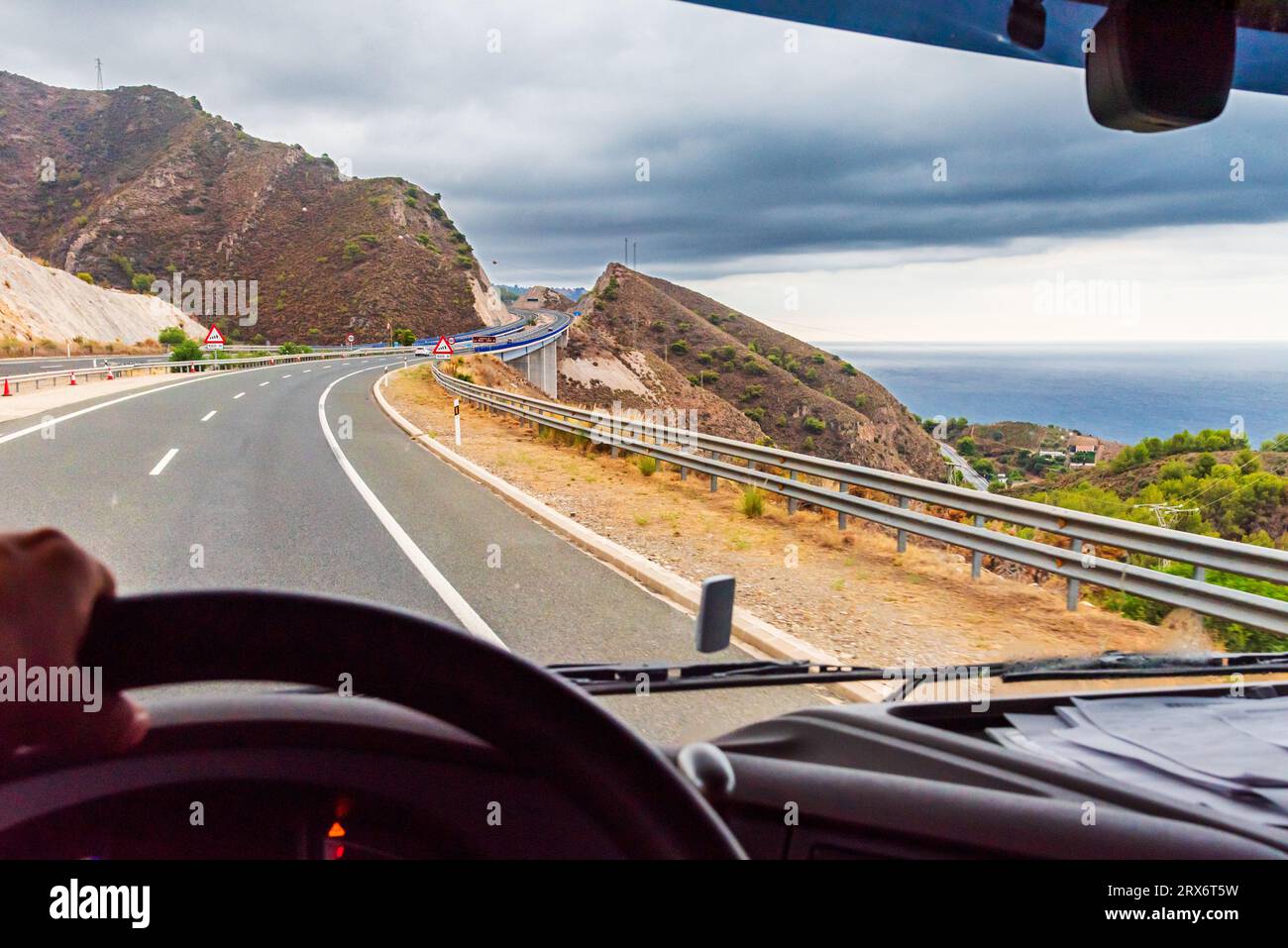 Blick aus der Fahrposition eines Lkws auf eine Autobahn, die zwischen Bergen verläuft. Stockfoto