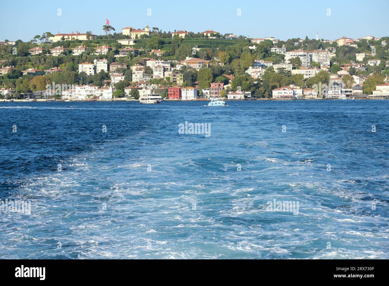 Wellen Sie Schaum hinter dem Boot auf dem Meer mit einem Stadthintergrund. Stockfoto
