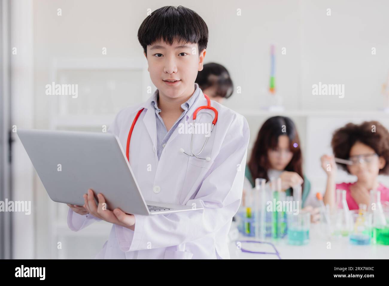 Porträt junger asiatischer chinesischer kluger Junge, der weiße Mantel warnt, spielt moderne Doktor mit Laptop-Computer und Freund Stockfoto