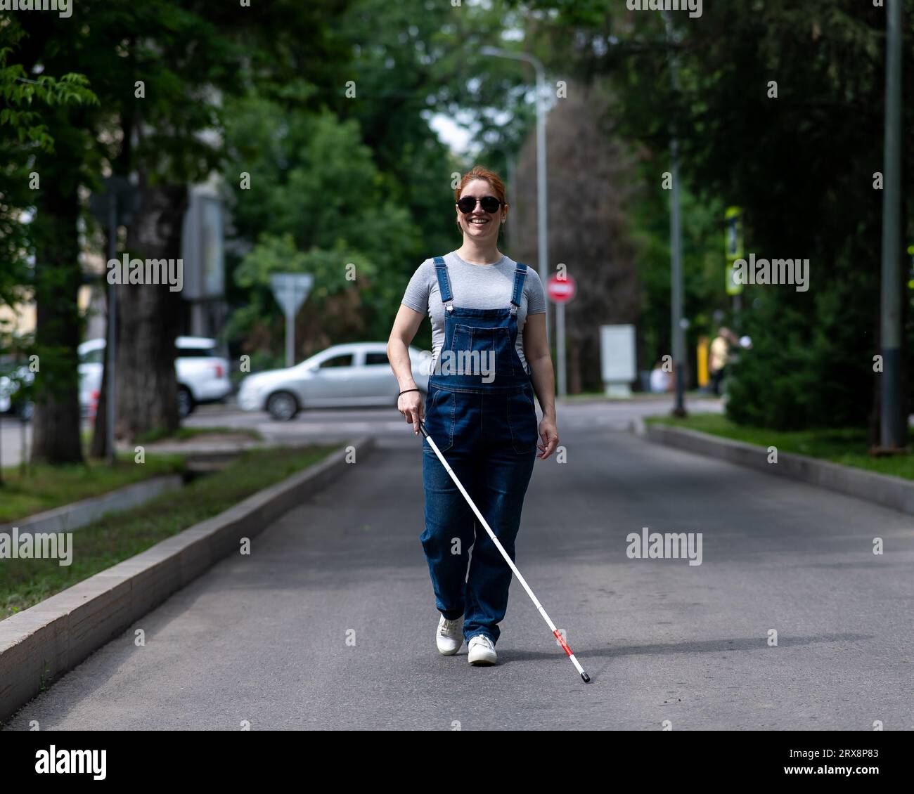 Blinde schwangere Frau, die mit einem Stock die Straße entlang läuft. Stockfoto