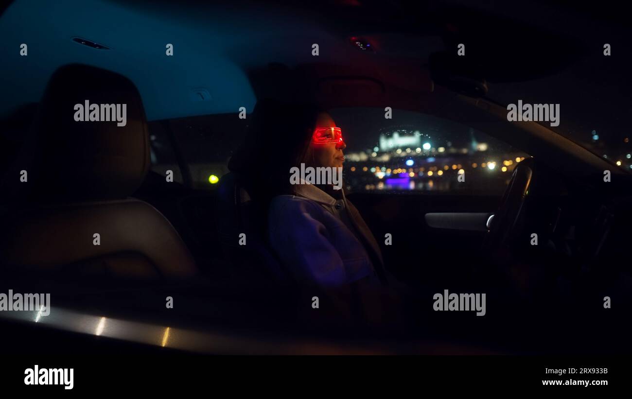 Junge schöne Frau benutzt Virtual-Reality-Brillen im Auto in der regnerischen Nacht Stockfoto