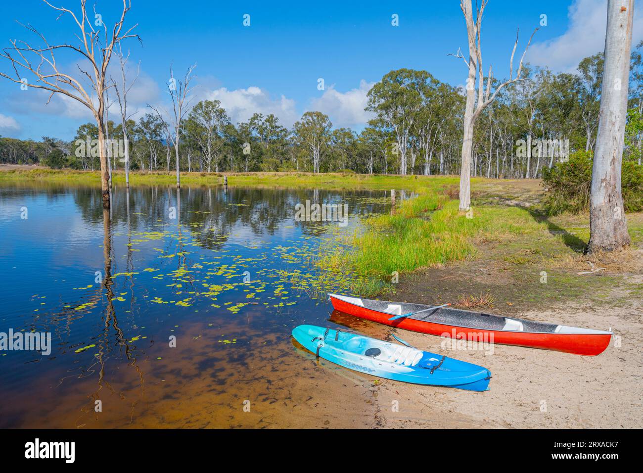 Kajaks auf dem Sandstrand des Süßwasserdamms mit Steg mit Ponton an sonnigen Tag im ländlichen Camp Aufenthalt. Childers Queensland, Australien Stockfoto