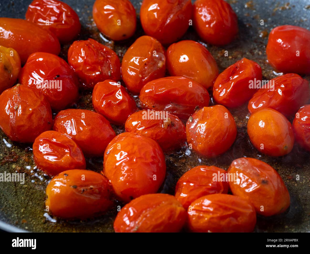 Nahaufnahme von Tomaten, die in Öl in einer Antihaftpfanne mit zerbrochenem schwarzem Pfeffer anbraten Stockfoto