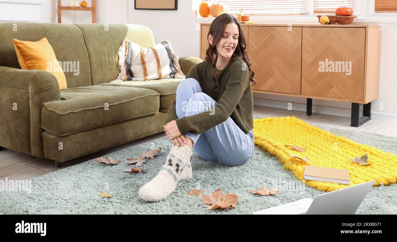 Junge Frau mit Laptop, die zu Hause am Herbsttag auf dem Teppich sitzt Stockfoto