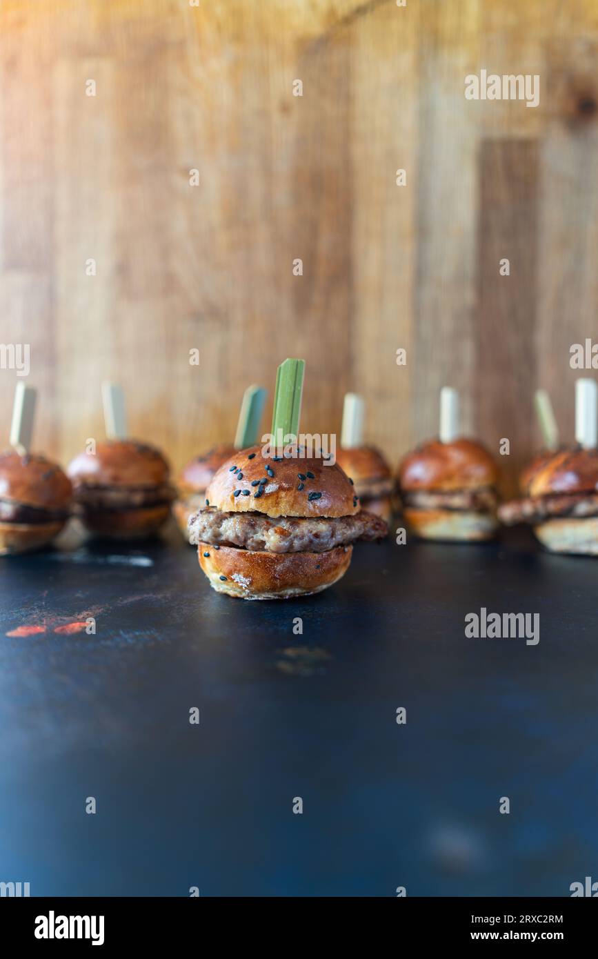 Mini-Burger auf hölzernen Zahnstochern, perfekt für Party-Snacks. Verschwommener Hintergrund in der Vorderansicht. Stockfoto