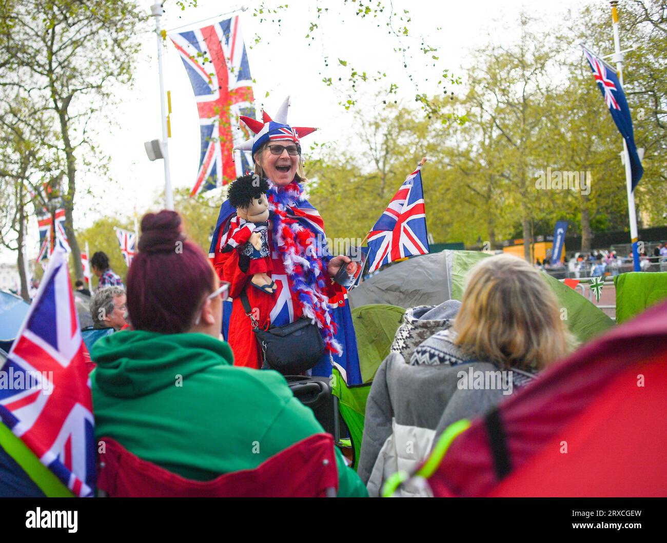 Eine Dame, die ein gestricktes Maskottchen hält und in Union Jack-Kleidung gekleidet ist, glücklich und lächelnd, mit einer Fahne auf der Mall London vor der Krönung von König Charles Stockfoto