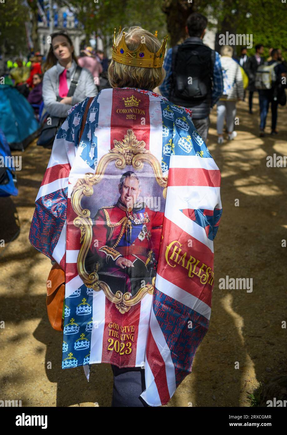 Eine Frau läuft mit einem Union Jack, der das Bild von König Charles über ihre Schultern trägt, während sie eine Krone auf der Mall London UK trägt. Krönung Stockfoto