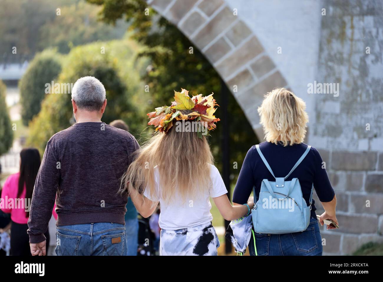 Erwachsenes Paar mit Tochter, die im Herbstpark spazieren geht. Ein Strauß Ahornblätter auf dem Mädchenkopf Stockfoto