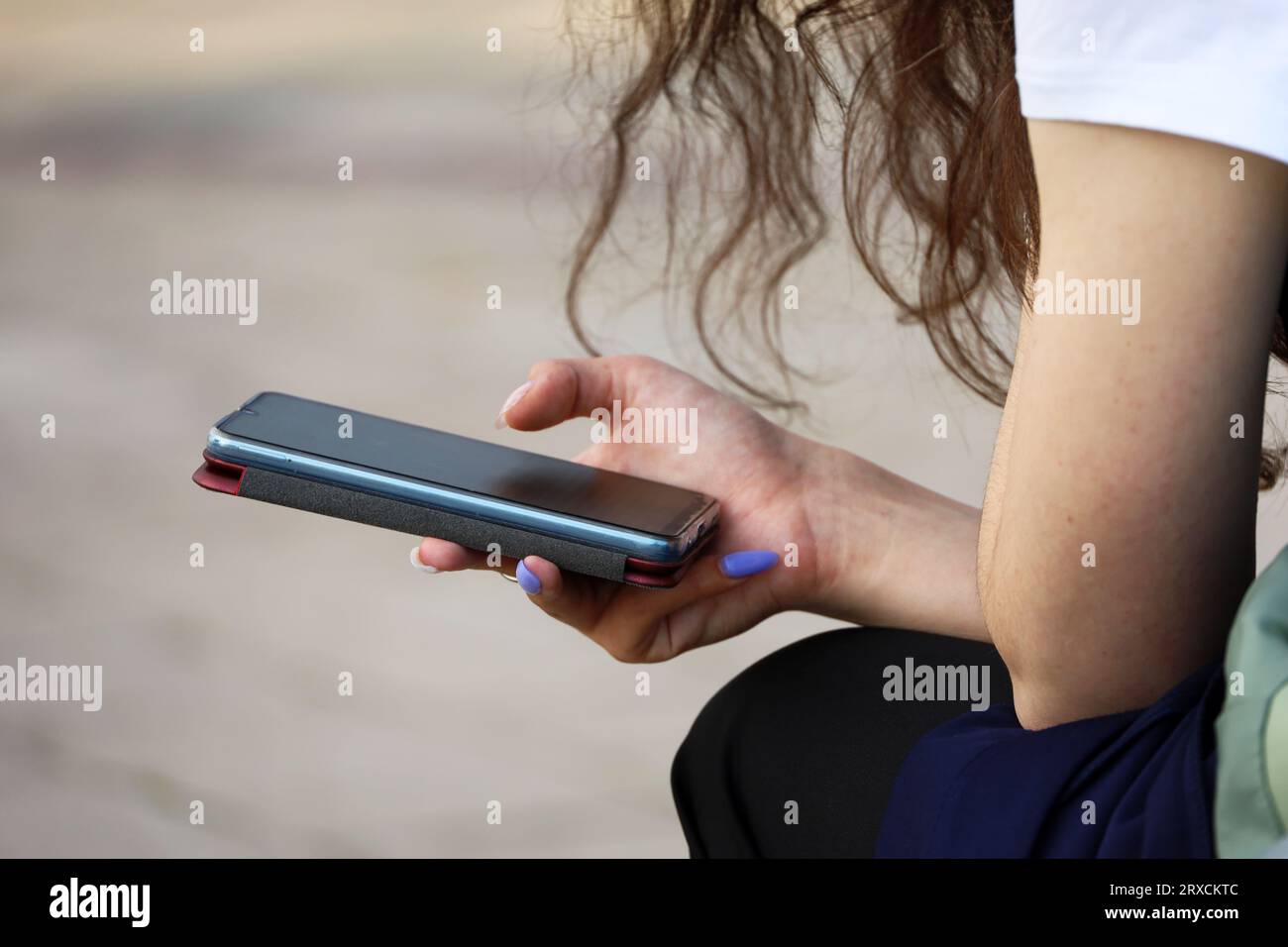Smartphone in weiblichen Händen aus nächster Nähe. Mädchen, das Handy benutzt, während sie auf der Straße sitzt Stockfoto