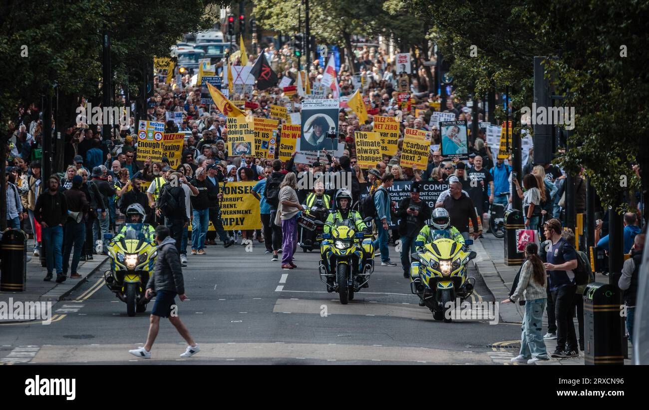 Polizei auf Motorrädern vor Menschenmassen, die durch London marschieren und gegen ULEZ und seine Expansion protestieren. Stockfoto