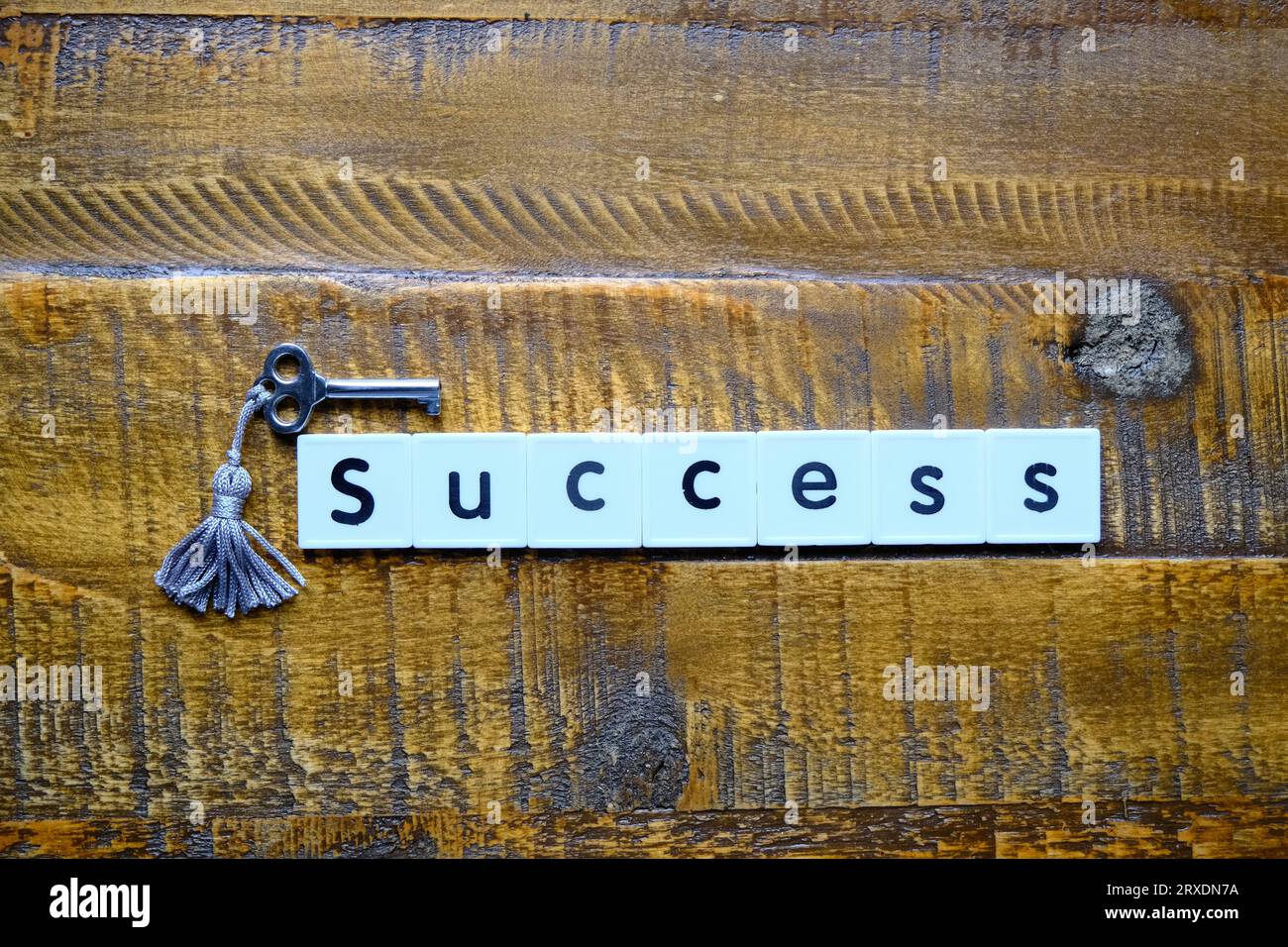 Ein Schlüssel auf einem Holztisch neben dem Wort „Erfolg“, das mit weißen Fliesenbuchstaben geschrieben ist Stockfoto
