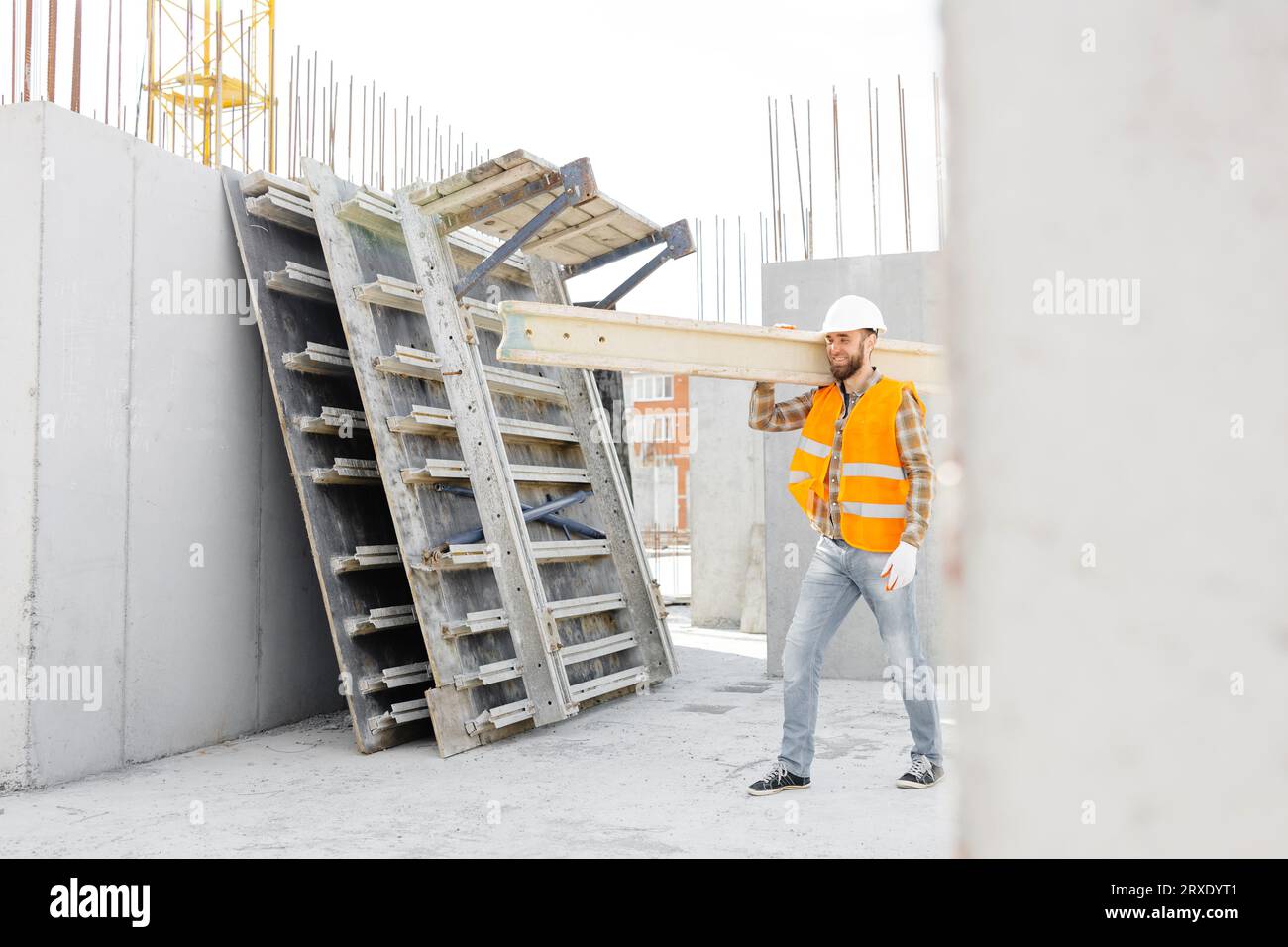 Bauarbeiter mit helm und weste trägt an seinem arbeitstag holz auf der  baustelle