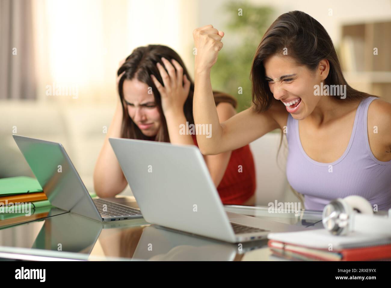 Der Schüler feiert den Erfolg und ein anderer beschwert sich, wenn er zu Hause Laptops überprüft Stockfoto
